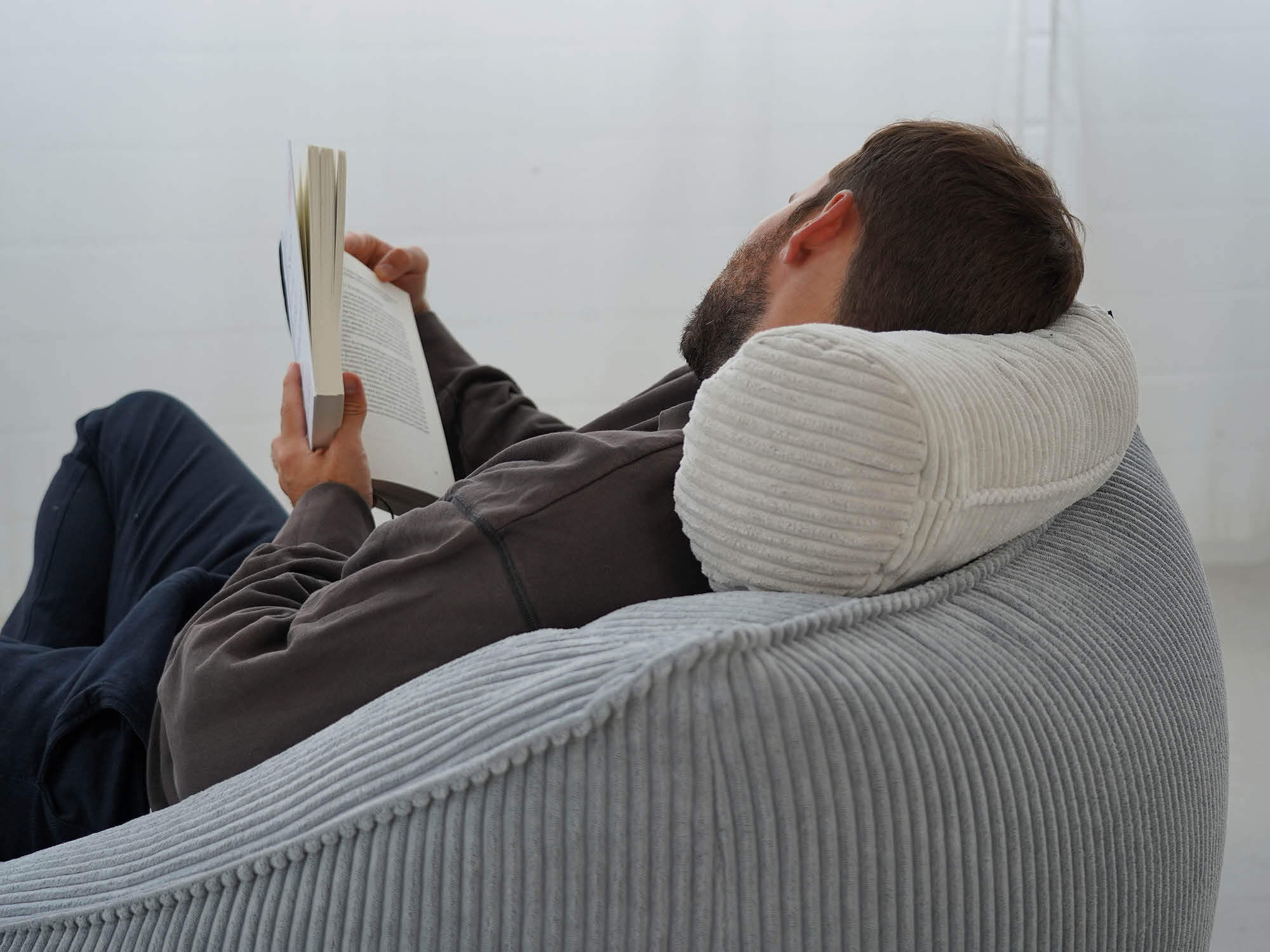 Nackenrolle aus Cord in beige auf Lehne eines Sitzsacks aus Cord im Nacken eines Mannes, Mann liest im Buch 