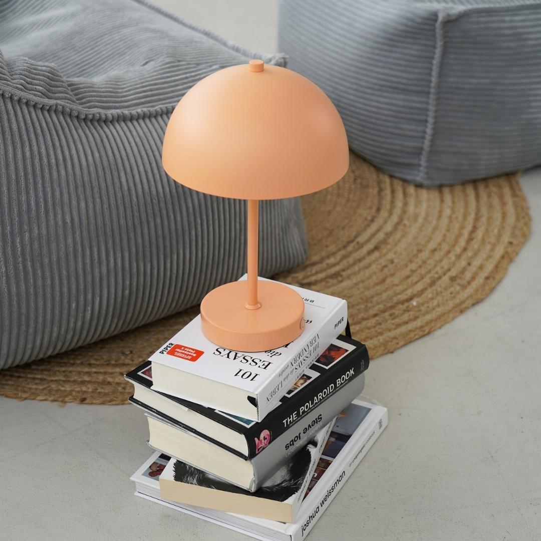 Kabellose LED Lampe in peach auf einem Stapel von Büchern. 