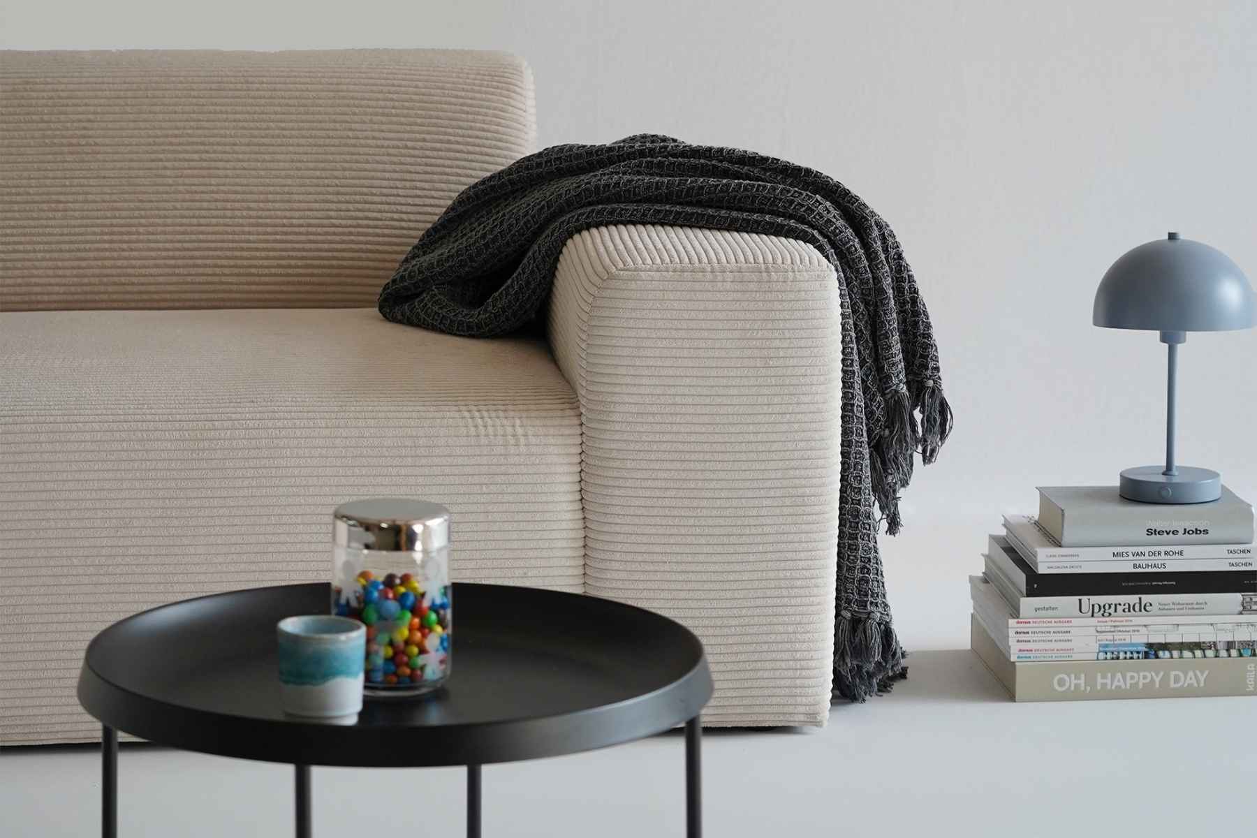 Sofa in Cord beige. rechte Armlehne über die eine Decke hängt 