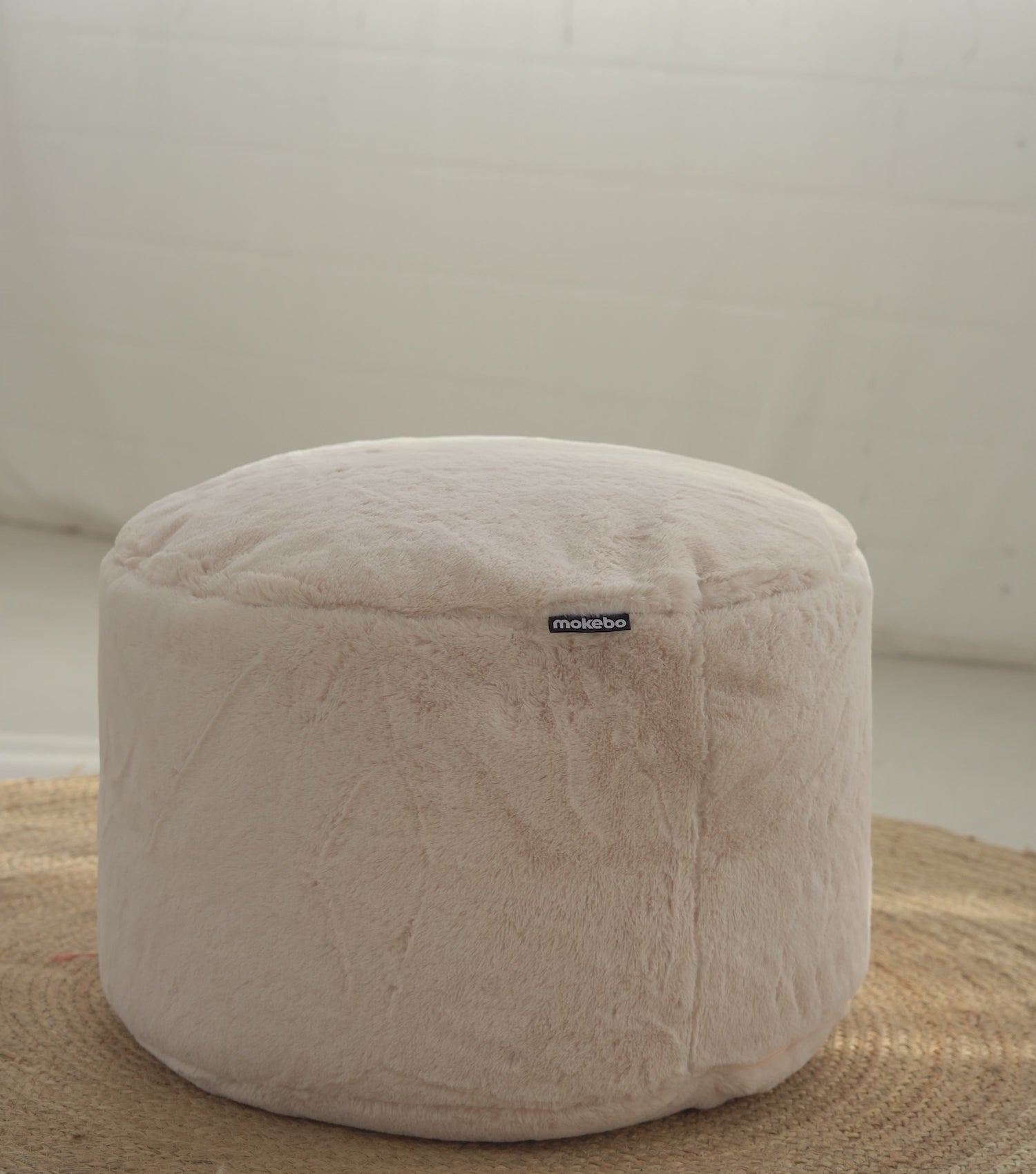 Produktvideo Pouf Sitzhocker mit weichem Kunstfell Stoff. Eine Decke, Lampe, Wolle und ein Tablett mit zwei Tassen werden hintereinander auf den Pouf gelegt. 