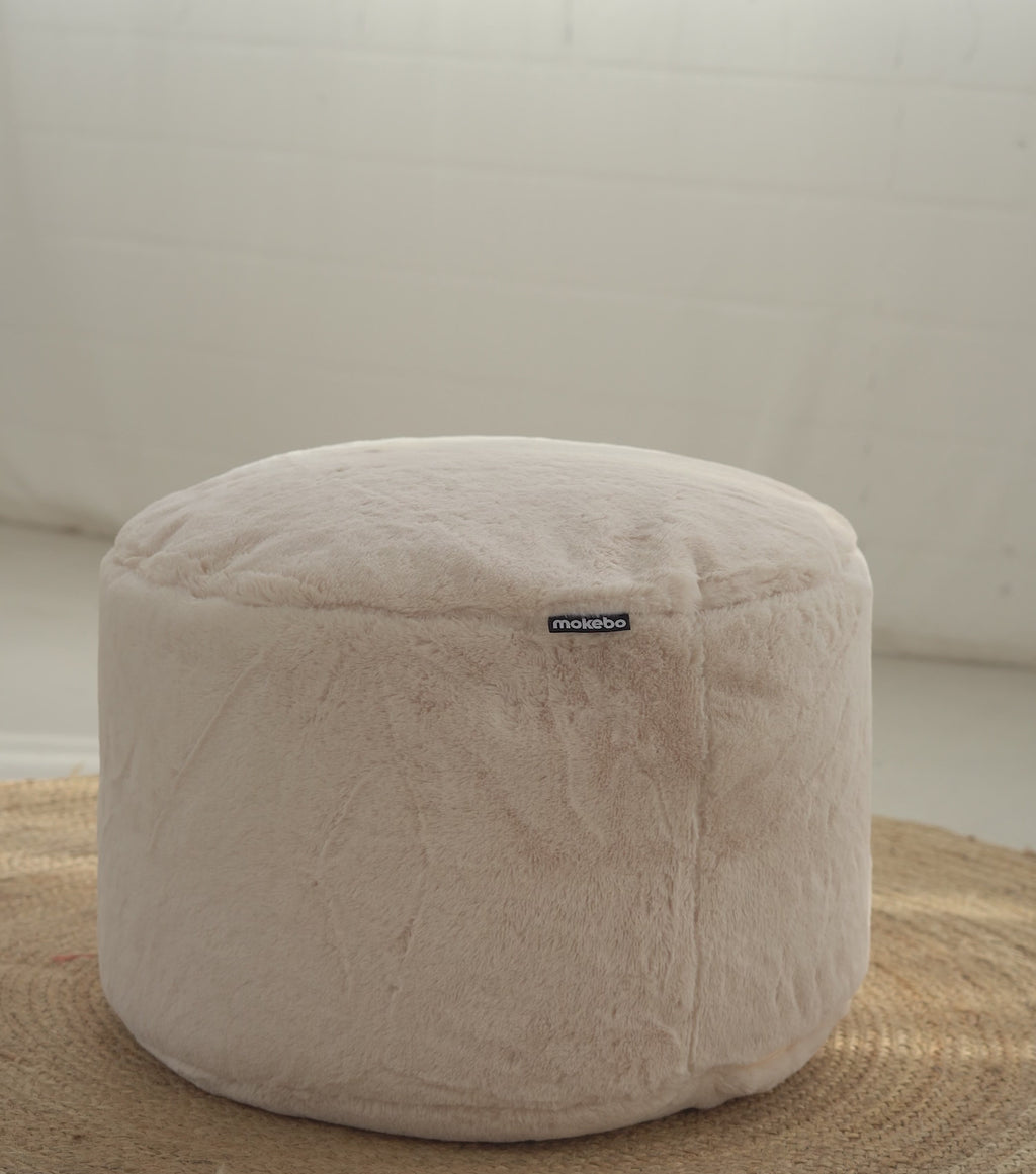 Produktvideo Pouf Sitzhocker mit weichem Kunstfell Stoff. Eine Decke, Lampe, Wolle und ein Tablett mit zwei Tassen werden hintereinander auf den Pouf gelegt. 